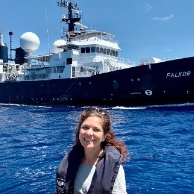 A woman smiles in front of a large ship